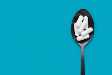 Capsules on black spoon against blue background