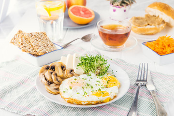Healthy breakfast plate with scrambled eggs, cheese, grilled mushrooms and sprout micro greens and other snacks and drinks on the served white wooden table. Selective focus.