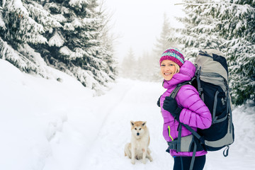 Happy woman walking in winter forest with dog