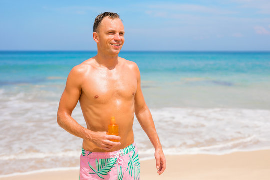 Man on the beach in bright sun holding sunscreen bottle in hand