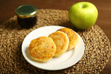Cheese pancake from cottage cheese are on a white plate. Nearby there is a glass jar with honey and an apple. Wooden background, woven backing. Proper nutrition. Dark background