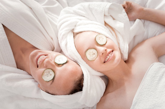 Fresh look. Happy nice positive mother and daughter lying together and smiling while doing a cucumber mask