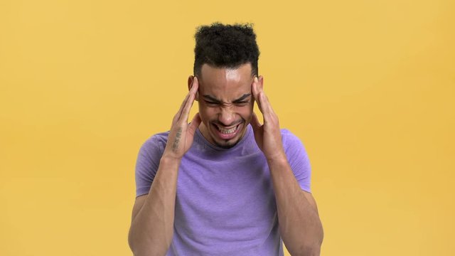Portrait of arabic young man rubbing temples having headache or suffering from migraine, isolated over yellow background. Concept of emotions