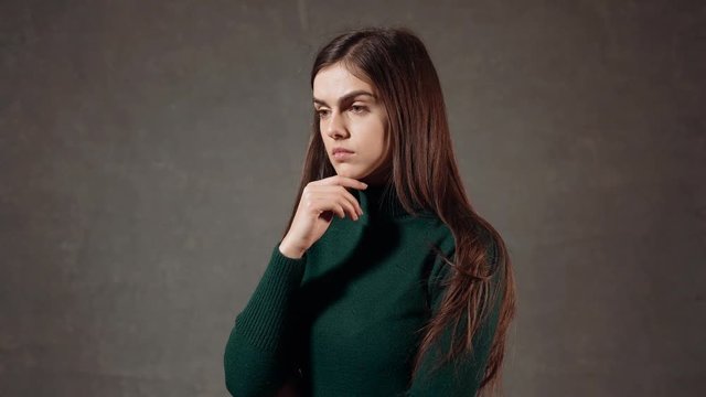 Portrait of a beautiful caucasian woman, wearing green turtleneck sweater, thinking seriously in the gray background
