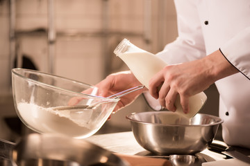 partial view of confectioner adding milk into dough in restaurant kitchen