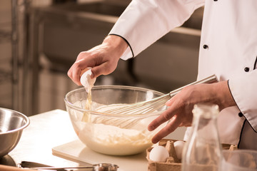 partial view of confectioner adding raw egg into dough in restaurant kitchen - obrazy, fototapety, plakaty
