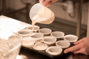 partial view of confectioner pouring dough into baking forms