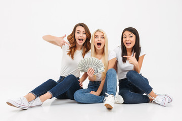 Three young cute pretty girls showing money pointing.