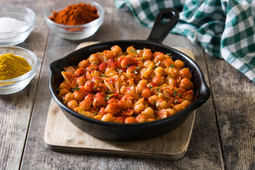 Fried spicy chickpeas in frying pan on wooden table