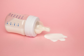 Baby milk bottle on a pink background with neagtive space. Spill