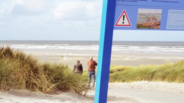 elderly couple passing a rip current advisory sign