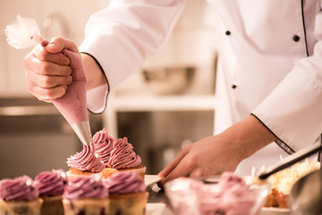 Cropped shot of confectioner putting cream on cupcakes - obrazy, fototapety, plakaty