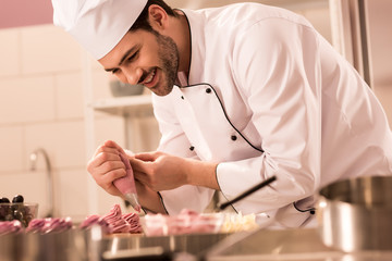  confectioner decorating cupcakes with cream in restaurant kitchen