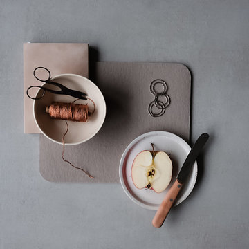 Overhead view of half apple on plate with scissors and spool on table