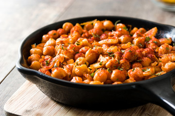 Fried spicy chickpeas in frying pan on wooden table
