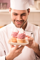 portrait of smiling confectioner looking at cupcakes on plate in hands