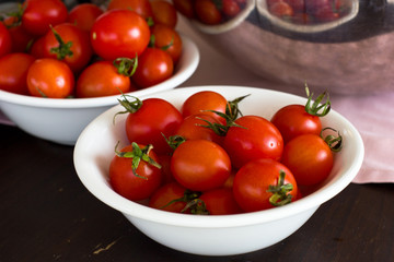 Whole cherry tomatoes in a white porcelain bowl on a brown wooden table