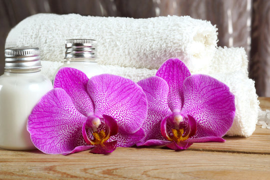 Pink orchid flowers near towels and white body lotion in the spa treatment room