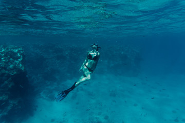 Underwater shot of the young woman gliding over vivid coral reef on a breath hold