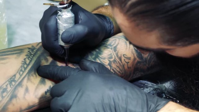 Master makes tattoo pictures in tattoo studio./Professional tattooist at work in tattoo parlor.