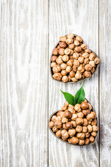Two heart shaped bowls with hazelnuts on white wooden background. Top view, copy space.