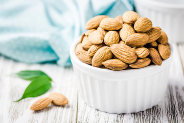 Almonds in white ceramic bowl on white wooden rustic background. Selective focus, copy space, closeup.