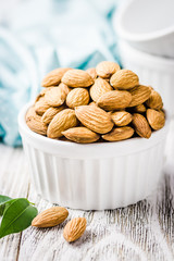 Almonds in white ceramic bowl on white wooden rustic background. Selective focus, copy space, closeup.