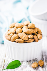 Almond nuts in white ceramic bowl on white wooden rustic background. Selective focus, copy space, closeup.