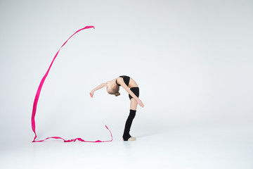 Rhythmic gymnastics caucasian blonde girl in black suite performing athelete exercises with pink ribbon handling abilities showing flexibility and acrobat balance on white background isolated