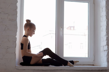 Rhythmic gymnastics caucasian ballet dancer girl in black suite sitting on a window sill rail in counterlight backgorund as ballerina