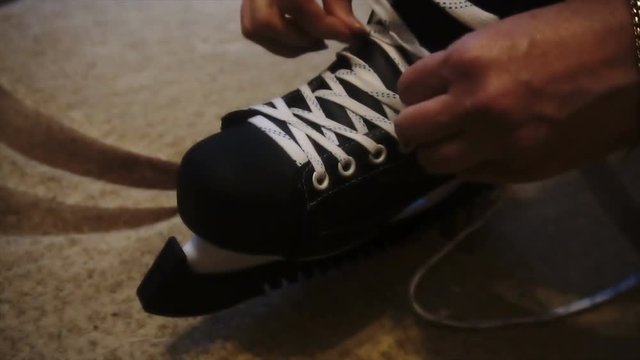 tying the white laces on skates,preparing to go on the ice.