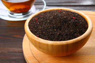 Black dry tea with a cherry in a bowl on a wooden table.