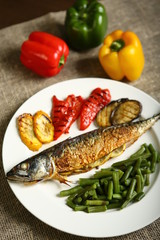 Healthy and proper food, grilled fish and vegetables with lemon and green beans on a white plate. On the background of pepper, burlap and wooden table. Low-calorie food. View from above