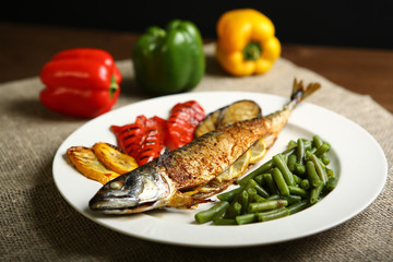 Healthy and proper food, grilled fish and vegetables with lemon and green beans on a white plate. On the background of pepper, burlap and wooden table. Low-calorie food