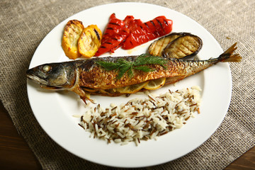 Healthy and proper food, grilled fish and vegetables with lemon and black and white rice on a white plate. Against the background of sacking and a wooden table. Low-calorie food