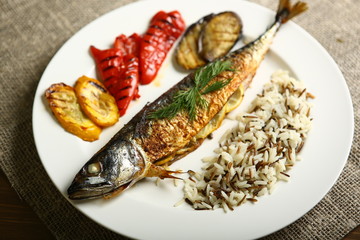 Healthy and proper food, grilled fish and vegetables with lemon and black and white rice on a white plate. Against the background of sacking and a wooden table. Low-calorie food