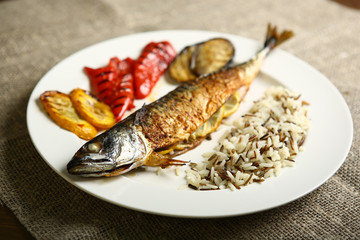 Healthy and proper food, grilled fish and vegetables with lemon and black and white rice on a white plate. Against the background of sacking and a wooden table. Low-calorie food