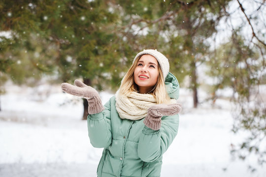 Young beautiful girl looks at falling snow and catches snowflakes. Portrait of an attractive girl on a winter background. Space for text.