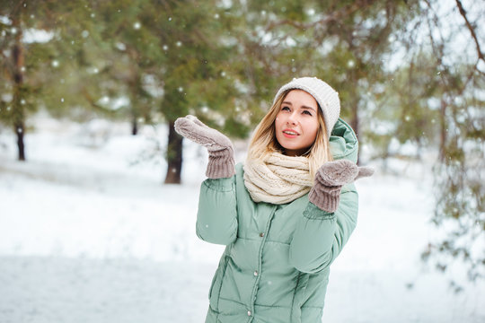 Young beautiful girl looks at falling snow and catches snowflakes. Portrait of an attractive girl on a winter background. Space for text.