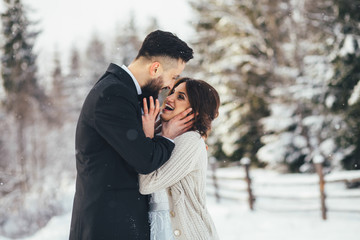 Bearded man and his lovely bride pose on the snow in a magic winter forest