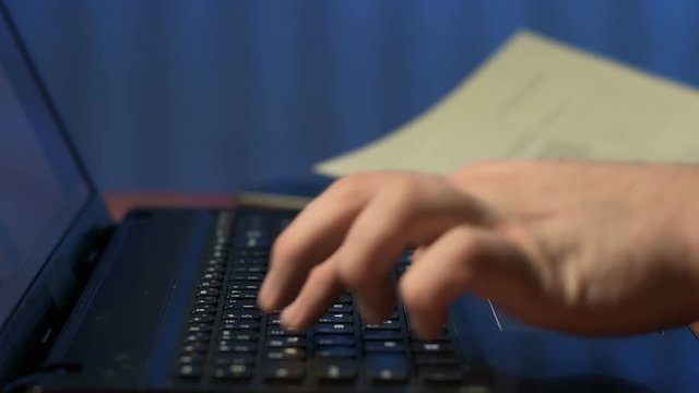 Closeup of man holding paper documents in his hand and presses keys of laptop at office