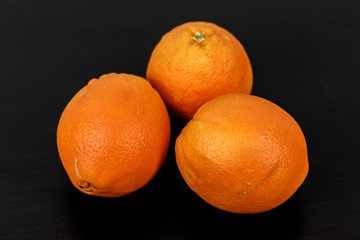 Drei Orangen auf schwarzem Hintergrund mit leichter Maserung
