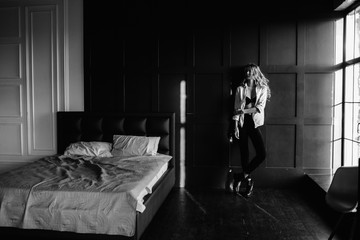 A girl with long blonde hair dressed in black jeans, a striped shirt and black shoes sitting on the bed with blue linens. Fashionable casual outfit.