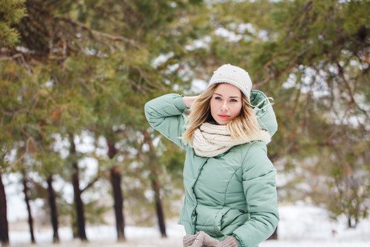 Young beautiful slender blonde girl outdoors in winter looking away. Portrait of an attractive model on a winter background. Space for text.