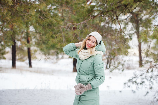 Young beautiful slender blonde girl smiles and looks at the camera outdoors in winter. Portrait of an attractive model on a winter background. Space for text.