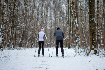 Photo from back of sports woman and man skiing in winter forest