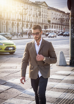Attractive man outdoor wearing elegant jacket, in European city, Turin in Italy, walking on zebra crossing