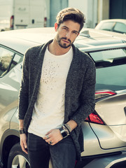 Portrait of young attractive man in white shirt leaning on his new stylish polished car outdoor in...