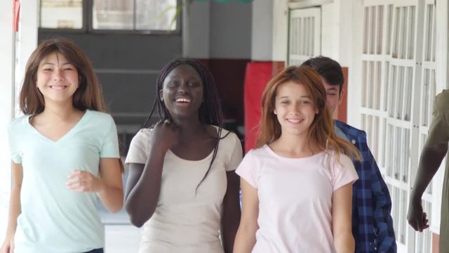 Happy group of mixed race teens walking in the school hallway happy and smiling