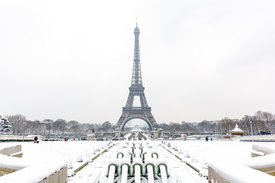 Winter in Paris in the snow. The Eiffel tower seen from the Trocadero garden with the water cannons of the Trocadero fountain covered in snow in the foreground.